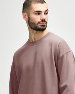 A model wearing a soft pink Gildan Softstyle adult sweatshirt. The sweatshirt features a classic fit and has a logo.