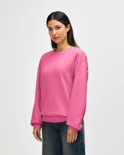 A pink Gildan Softstyle adult sweatshirt displayed on a model, featuring long sleeves and a crew neckline.