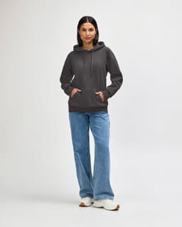 A woman wears a grey hooded sweatshirt with a logo, paired with denim jeans and white sneakers.