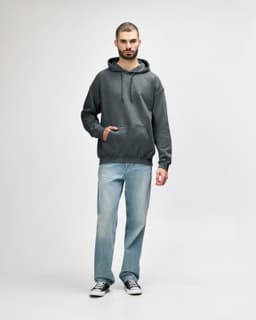 A green Gildan Softstyle adult hooded sweatshirt worn by a model, paired with dark jeans and sneakers.
