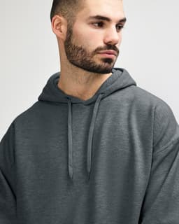 A soft grey hooded sweatshirt, featuring a front pocket and a hood, worn by a model. It has a small logo.