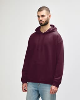 A burgundy adult hooded sweatshirt, featuring a front pocket and a drawstring hood. The model stands casually.