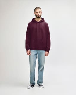 A woman is wearing a burgundy hooded sweatshirt paired with blue jeans and white sneakers. The sweatshirt has a logo.