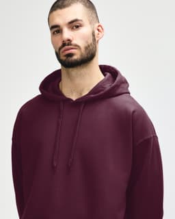 A woman models a burgundy Gildan Softstyle adult hooded sweatshirt with a drawstring hood and a subtle logo.