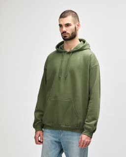 A green Gildan Softstyle adult hooded sweatshirt worn by a model, featuring a front pocket and a drawstring hood.