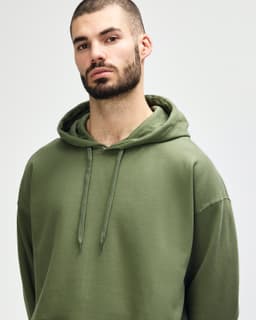 A model wearing a green Gildan Softstyle adult hooded sweatshirt, featuring a hood and drawstrings.