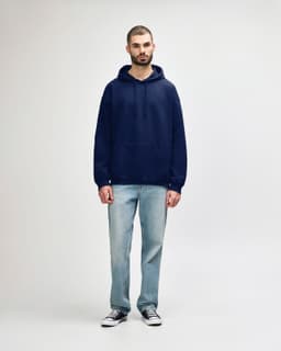 A model wearing a navy hooded sweatshirt and blue jeans, featuring a front pocket and a logo.