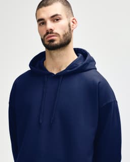 A woman wearing a navy blue hooded sweatshirt, with a relaxed expression, holding the hood. The sweatshirt has a logo.