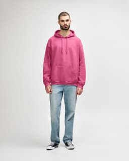 A pink hooded sweatshirt featuring a front pocket, paired with blue jeans and white sneakers.