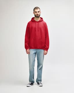 A red Gildan Softstyle adult hooded sweatshirt worn by a model, paired with blue jeans and white shoes.