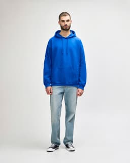 A blue adult hooded sweatshirt featuring a front pocket, worn by a model alongside black jeans and sneakers.