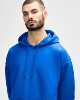 A blue Gildan Softstyle adult hooded sweatshirt worn by a model adjusting the hood. The sweatshirt has a logo.