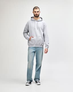 A man stands wearing a grey Gildan Softstyle hooded sweatshirt and light blue jeans, with a logo on the sweatshirt.