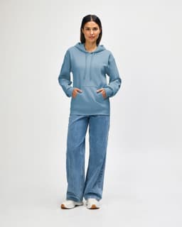 A blue hooded sweatshirt worn by a model, paired with jeans and sneakers, featuring a logo.