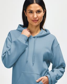 A hooded sweatshirt in a soft blue shade, featuring a drawstring and a relaxed fit, worn by a model.