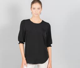 A black top with shirred cuffs, featuring a round neckline and a relaxed fit. The model is styled against a grey background.