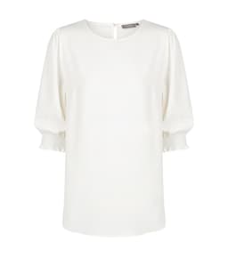 A white blouse with shirred cuffs and a round neckline, featuring a button closure at the back and a brand logo.