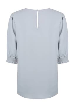 A light blue top with shirred cuffs and a keyhole back detail. It has a smooth, flowing design and includes branding.