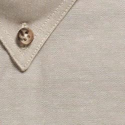 A close-up of a beige work shirt featuring a collar and a button. The fabric has a textured finish.