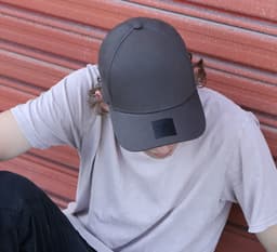 A grey cotton/spandex cap featuring a logo, worn by a person sitting against a red background.