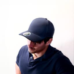 A navy blue cap with a circular logo, worn by a man in a dark polo shirt, angled downwards.