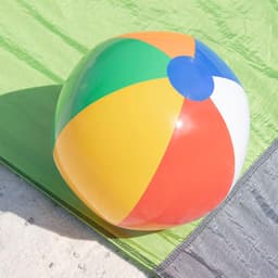 A colourful inflatable beach ball featuring red, yellow, green, and blue panels on a sandy surface.