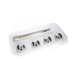 A set of four stainless steel ice stones and a tong, presented in a clear tray. The ice stones are silver.