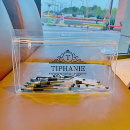 A clear PVC zipper bag containing various small metal items, with a decorative logo on the front.