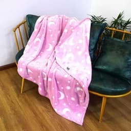 A pink glow-in-the-dark blanket featuring moon and star patterns, draped over a green sofa.