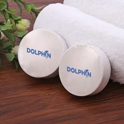 Two round white compressed towels with a logo on them, placed on a wooden surface alongside a rolled white towel and leaves.