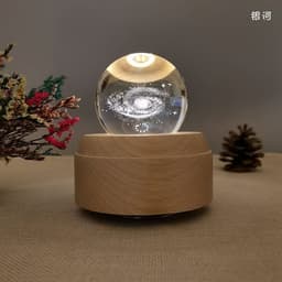 A crystal ball night light with a wooden base, featuring a galaxy design inside. Surrounding decorations include pinecones and foliage.