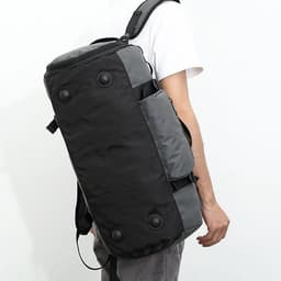 A foldable travel duffel bag in black and grey, carried on the shoulder of a person against a plain background.