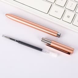 A rose gold custom writing pen displayed alongside its components, resting on a white surface next to a keyboard.