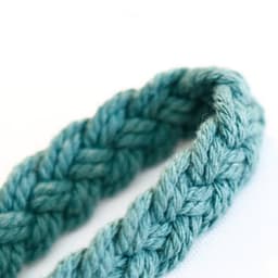 A braided, teal macrame wrist strap, showcasing a textured design and soft, durable fibres. It features a logo.