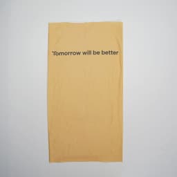A yellow multifunctional neck gaiter with a motivational phrase printed on it. It features a logo.