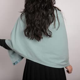 A solid colour button shawl in soft blue worn over a black outfit, showcasing its draped design.