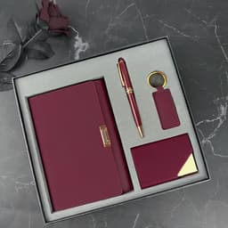 A burgundy gift set featuring a notebook, pen, keyring, and cardholder, presented in a sleek box with a soft interior.