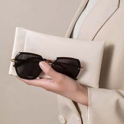 A hand holds a black pair of sunglasses alongside a cream-coloured storage bag. The bag features a logo.