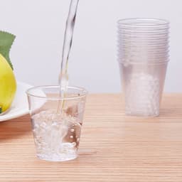 A clear plastic party cup being filled with liquid, with stacked cups visible in the background.