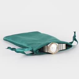 A teal velvet gift bag with a watch partially visible inside, featuring a decorative drawstring closure.