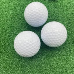 Three white golf balls on a green grass surface, featuring a textured surface.