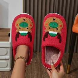 Red fuzzy slippers featuring a reindeer design with green and brown accents, displayed with a person's hands.
