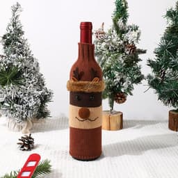 A drink bottle covered in a brown knitted sleeve with a reindeer design, set among miniature Christmas trees.