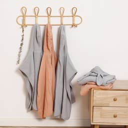 A set of baby hooded poncho towels in grey and peach hanging on a wall, with a folded towel beside a wooden dresser.