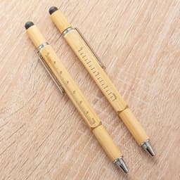 A multifunctional ballpoint pen made of bamboo, featuring a silver clip and black rubber tip, displayed on a wooden surface.