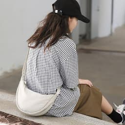 A person wearing a checkered shirt and skirt sits, showcasing a light-coloured personalized crossbody bag.