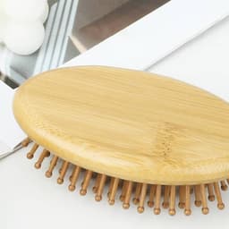 A bamboo massage comb with rounded edges and wooden bristles on a flat surface, surrounded by neutral tones.