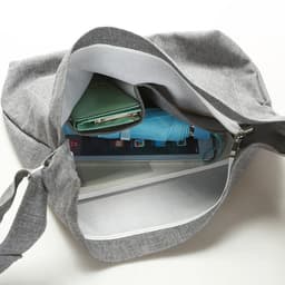 A grey canvas shoulder bag with a visible interior containing a tablet, a wallet, and a drink bottle.