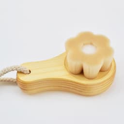 A flower-shaped wooden facial cleansing brush with soft bristles, featuring a natural wood handle and a rope.