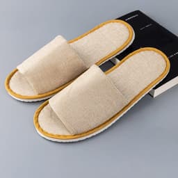 Open toe cotton disposable slippers in beige with a yellow trim, positioned next to a black book.